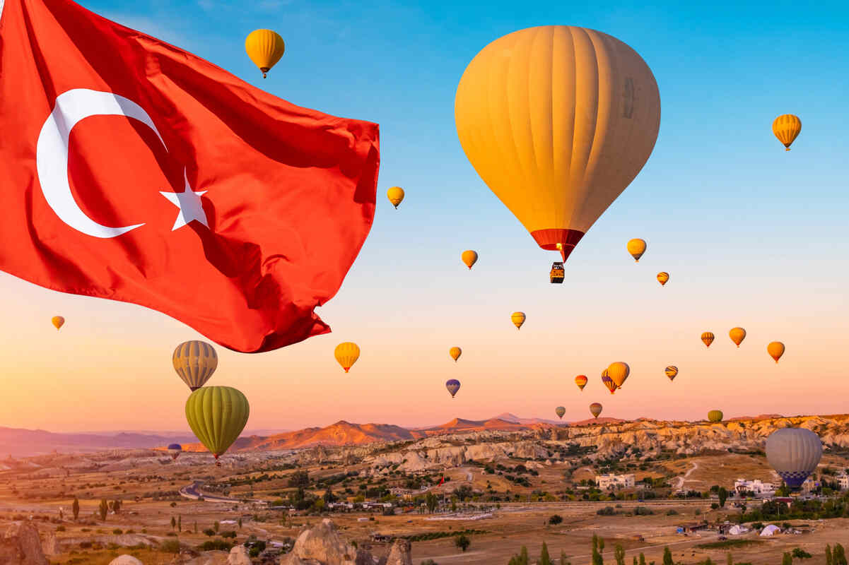 Hot air balloons at sunrise with a Turkish flag in the foreground