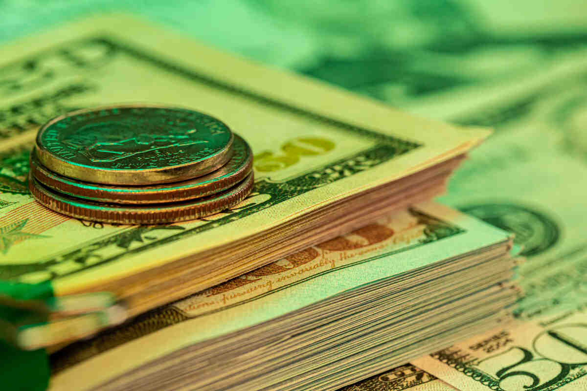 Fifty-dollar bills with coins on top against a blurred money background.