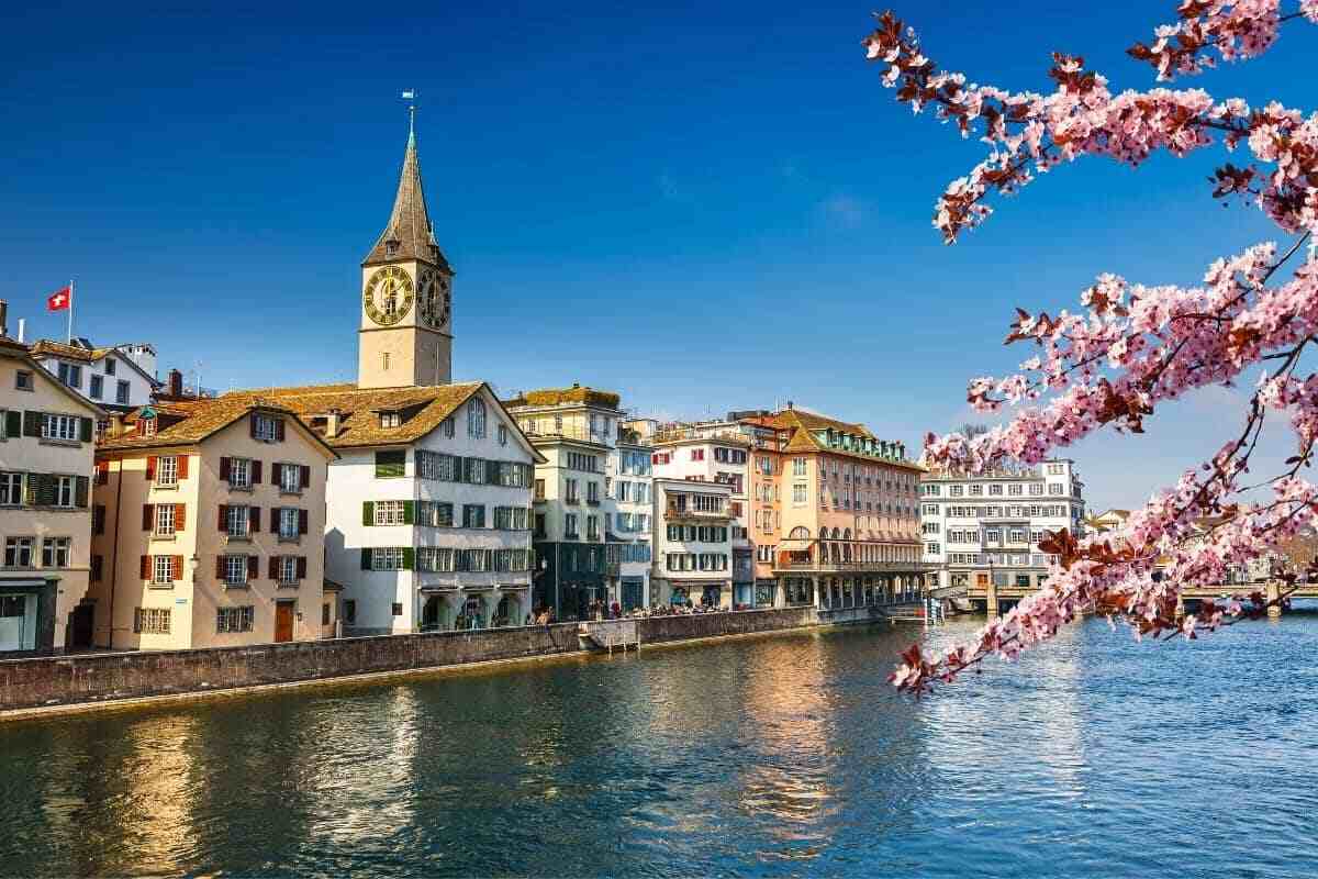 Spring in Switzerland: cherry blossoms, a river, and a clock tower under a blue sky.