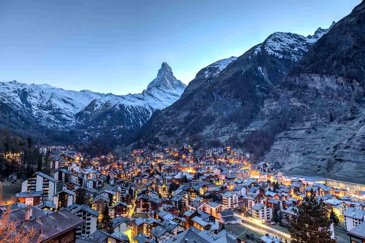 Swiss village at dusk with snow-capped Matterhorn and surrounding serene valley.